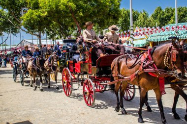 Seville, İspanya - 1 Mayıs 2022 Sevillianlar geleneksel Endülüs tarzında giyinmiş bir at arabasıyla İspanya 'nın en ünlü festivali olan Feria de Sevilla' nın koridorlarında dolaşıyorlar.