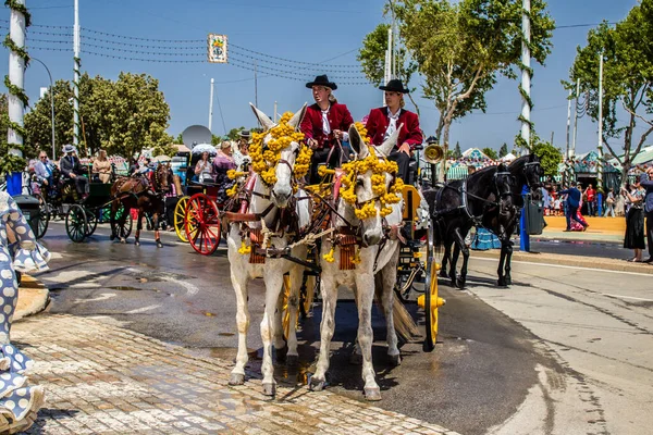 Seville, İspanya - 1 Mayıs 2022 Sevillianlar geleneksel Endülüs tarzında giyinmiş bir at arabasıyla İspanya 'nın en ünlü festivali olan Feria de Sevilla' nın koridorlarında dolaşıyorlar.