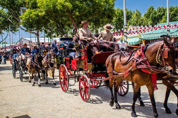 Севилья, Испания - 01 мая 2022 года Севилья, одетые в традиционный андалузский стиль верховой езды в конном экипаже через проходы Feria de Sevilla, самый известный фестиваль в Испании