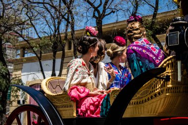 Seville, İspanya... 1 Mayıs 2022 Sevilla 'lılar geleneksel Endülüs tarzında giyinip Seville sokaklarında at arabasıyla geziyorlar.