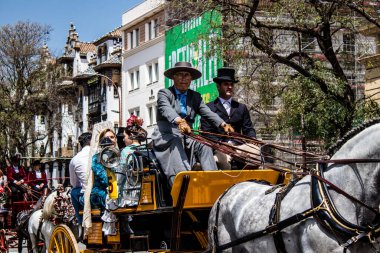 Seville, İspanya... 1 Mayıs 2022 Sevilla 'lılar geleneksel Endülüs tarzında giyinip Seville sokaklarında at arabasıyla geziyorlar.