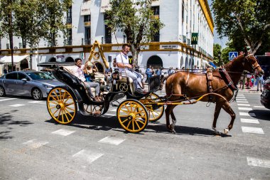 Seville, Spain- May 01, 2022 Sevillians dressed in traditional Andalusian way riding in a carriage with horses through the streets of Seville, celebration  back after two years of absence due to covid