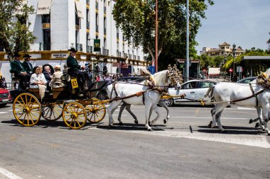 Seville, İspanya... 1 Mayıs 2022 Sevilla 'lılar geleneksel Endülüs tarzında giyinip Seville sokaklarında at arabasıyla geziyorlar.
