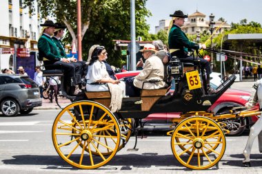 Seville, İspanya... 1 Mayıs 2022 Sevilla 'lılar geleneksel Endülüs tarzında giyinip Seville sokaklarında at arabasıyla geziyorlar.
