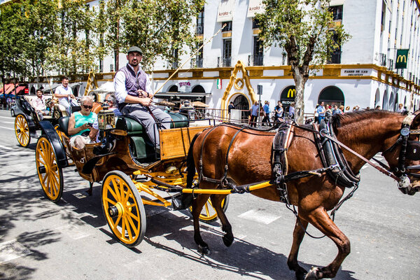 Seville, Spain- May 01, 2022 Sevillians dressed in traditional Andalusian way riding in a carriage with horses through the streets of Seville, celebration  back after two years of absence due to covid