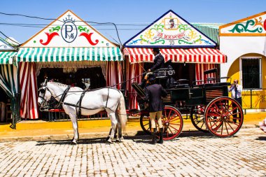 Seville, İspanya - 5 Mayıs 2022 Sevillianlar geleneksel Endülüs tarzında giyinmiş bir şekilde İspanya 'nın en ünlü festivali olan Feria de Sevilla' nın koridorlarında at arabasıyla dolaşıyorlar.
