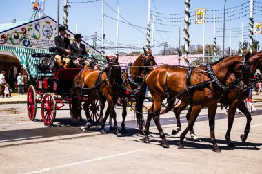 Seville, İspanya - 5 Mayıs 2022 Sevillianlar geleneksel Endülüs tarzında giyinmiş bir şekilde İspanya 'nın en ünlü festivali olan Feria de Sevilla' nın koridorlarında at arabasıyla dolaşıyorlar.