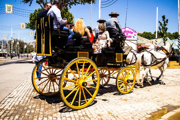 Seville, İspanya - 5 Mayıs 2022 Sevillianlar geleneksel Endülüs tarzında giyinmiş bir şekilde İspanya 'nın en ünlü festivali olan Feria de Sevilla' nın koridorlarında at arabasıyla dolaşıyorlar.