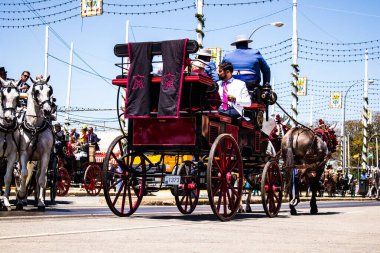 Seville, İspanya - 5 Mayıs 2022 Sevillianlar geleneksel Endülüs tarzında giyinmiş bir şekilde İspanya 'nın en ünlü festivali olan Feria de Sevilla' nın koridorlarında at arabasıyla dolaşıyorlar.
