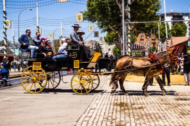 Seville, İspanya - 5 Mayıs 2022 Sevillianlar geleneksel Endülüs tarzında giyinmiş bir şekilde İspanya 'nın en ünlü festivali olan Feria de Sevilla' nın koridorlarında at arabasıyla dolaşıyorlar.