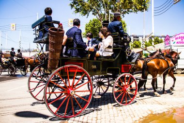 Seville, İspanya - 5 Mayıs 2022 Sevillianlar geleneksel Endülüs tarzında giyinmiş bir şekilde İspanya 'nın en ünlü festivali olan Feria de Sevilla' nın koridorlarında at arabasıyla dolaşıyorlar.