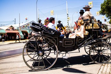 Seville, İspanya - 5 Mayıs 2022 Sevillianlar geleneksel Endülüs tarzında giyinmiş bir şekilde İspanya 'nın en ünlü festivali olan Feria de Sevilla' nın koridorlarında at arabasıyla dolaşıyorlar.
