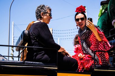 Seville, Spain - May 05, 2022 Sevillians dressed in the traditional Andalusian way riding in a horse drawn carriage through the aisles of the Feria de Sevilla, the most famous festival in Spain
