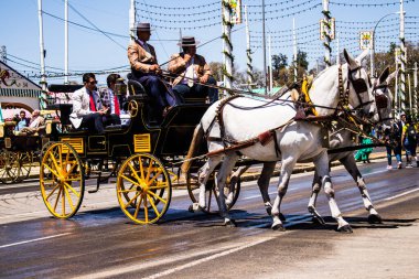 Seville, İspanya - 5 Mayıs 2022 Sevillianlar geleneksel Endülüs tarzında giyinmiş bir şekilde İspanya 'nın en ünlü festivali olan Feria de Sevilla' nın koridorlarında at arabasıyla dolaşıyorlar.