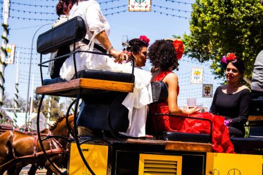 Seville, İspanya - 5 Mayıs 2022 Sevillianlar geleneksel Endülüs tarzında giyinmiş bir şekilde İspanya 'nın en ünlü festivali olan Feria de Sevilla' nın koridorlarında at arabasıyla dolaşıyorlar.