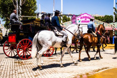 Seville, İspanya - 5 Mayıs 2022 Sevillianlar geleneksel Endülüs tarzında giyinmiş bir şekilde İspanya 'nın en ünlü festivali olan Feria de Sevilla' nın koridorlarında at arabasıyla dolaşıyorlar.