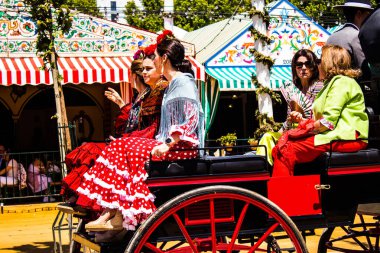 Seville, İspanya - 5 Mayıs 2022 Sevillianlar geleneksel Endülüs tarzında giyinmiş bir şekilde İspanya 'nın en ünlü festivali olan Feria de Sevilla' nın koridorlarında at arabasıyla dolaşıyorlar.