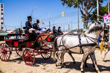 Seville, İspanya - 5 Mayıs 2022 Sevillianlar geleneksel Endülüs tarzında giyinmiş bir şekilde İspanya 'nın en ünlü festivali olan Feria de Sevilla' nın koridorlarında at arabasıyla dolaşıyorlar.