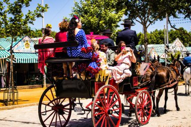 Seville, İspanya - 5 Mayıs 2022 Sevillianlar geleneksel Endülüs tarzında giyinmiş bir şekilde İspanya 'nın en ünlü festivali olan Feria de Sevilla' nın koridorlarında at arabasıyla dolaşıyorlar.