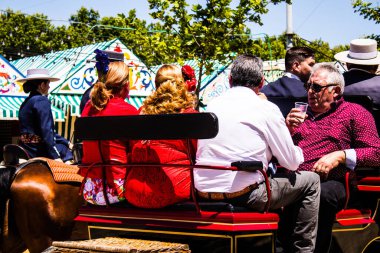 Seville, İspanya - 5 Mayıs 2022 Sevillianlar geleneksel Endülüs tarzında giyinmiş bir şekilde İspanya 'nın en ünlü festivali olan Feria de Sevilla' nın koridorlarında at arabasıyla dolaşıyorlar.