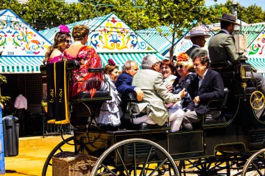 Seville, İspanya - 5 Mayıs 2022 Sevillianlar geleneksel Endülüs tarzında giyinmiş bir şekilde İspanya 'nın en ünlü festivali olan Feria de Sevilla' nın koridorlarında at arabasıyla dolaşıyorlar.