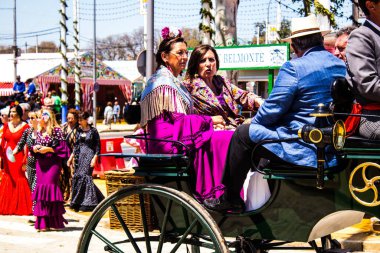 Seville, İspanya - 5 Mayıs 2022 Sevillianlar geleneksel Endülüs tarzında giyinmiş bir şekilde İspanya 'nın en ünlü festivali olan Feria de Sevilla' nın koridorlarında at arabasıyla dolaşıyorlar.