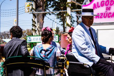 Seville, İspanya - 5 Mayıs 2022 Sevillianlar geleneksel Endülüs tarzında giyinmiş bir şekilde İspanya 'nın en ünlü festivali olan Feria de Sevilla' nın koridorlarında at arabasıyla dolaşıyorlar.