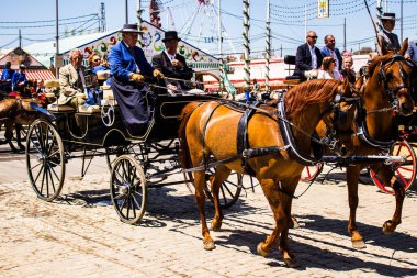 Seville, Spain - May 05, 2022 Sevillians dressed in the traditional Andalusian way riding in a horse drawn carriage through the aisles of the Feria de Sevilla, the most famous festival in Spain