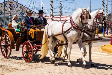 Seville, İspanya - 5 Mayıs 2022 Sevillianlar geleneksel Endülüs tarzında giyinmiş bir şekilde İspanya 'nın en ünlü festivali olan Feria de Sevilla' nın koridorlarında at arabasıyla dolaşıyorlar.