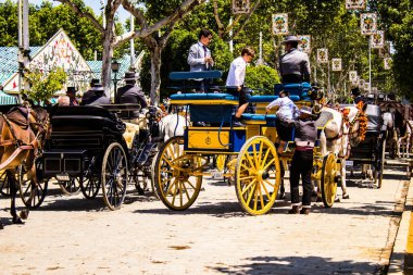 Seville, İspanya - 5 Mayıs 2022 Sevillianlar geleneksel Endülüs tarzında giyinmiş bir şekilde İspanya 'nın en ünlü festivali olan Feria de Sevilla' nın koridorlarında at arabasıyla dolaşıyorlar.