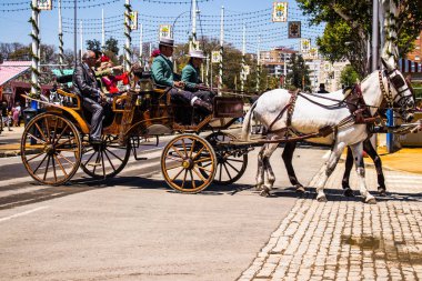 Seville, Spain - May 05, 2022 Sevillians dressed in the traditional Andalusian way riding in a horse drawn carriage through the aisles of the Feria de Sevilla, the most famous festival in Spain