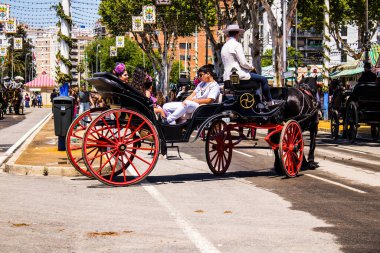 Seville, İspanya - 5 Mayıs 2022 Sevillianlar geleneksel Endülüs tarzında giyinmiş bir şekilde İspanya 'nın en ünlü festivali olan Feria de Sevilla' nın koridorlarında at arabasıyla dolaşıyorlar.