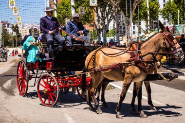 Seville, İspanya - 5 Mayıs 2022 Sevillianlar geleneksel Endülüs tarzında giyinmiş bir şekilde İspanya 'nın en ünlü festivali olan Feria de Sevilla' nın koridorlarında at arabasıyla dolaşıyorlar.
