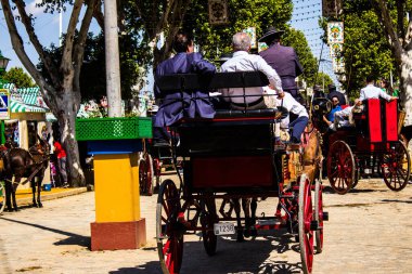 Seville, İspanya - 5 Mayıs 2022 Sevillianlar geleneksel Endülüs tarzında giyinmiş bir şekilde İspanya 'nın en ünlü festivali olan Feria de Sevilla' nın koridorlarında at arabasıyla dolaşıyorlar.