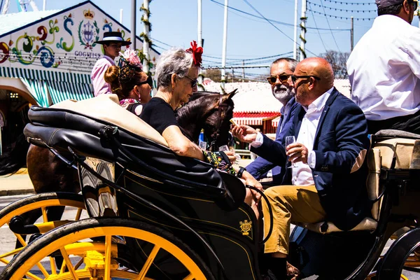 Seville, İspanya - 5 Mayıs 2022 Sevillianlar geleneksel Endülüs tarzında giyinmiş bir şekilde İspanya 'nın en ünlü festivali olan Feria de Sevilla' nın koridorlarında at arabasıyla dolaşıyorlar.