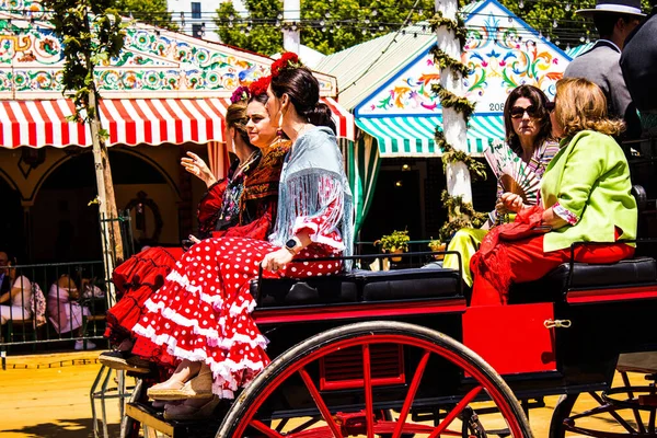 Seville, İspanya - 5 Mayıs 2022 Sevillianlar geleneksel Endülüs tarzında giyinmiş bir şekilde İspanya 'nın en ünlü festivali olan Feria de Sevilla' nın koridorlarında at arabasıyla dolaşıyorlar.