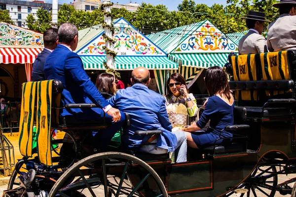 Seville, İspanya - 5 Mayıs 2022 Sevillianlar geleneksel Endülüs tarzında giyinmiş bir şekilde İspanya 'nın en ünlü festivali olan Feria de Sevilla' nın koridorlarında at arabasıyla dolaşıyorlar.