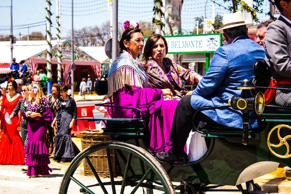 Seville, İspanya - 5 Mayıs 2022 Sevillianlar geleneksel Endülüs tarzında giyinmiş bir şekilde İspanya 'nın en ünlü festivali olan Feria de Sevilla' nın koridorlarında at arabasıyla dolaşıyorlar.