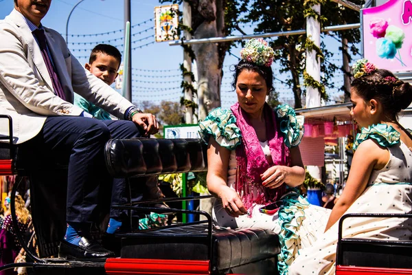 Seville, İspanya - 5 Mayıs 2022 Sevillianlar geleneksel Endülüs tarzında giyinmiş bir şekilde İspanya 'nın en ünlü festivali olan Feria de Sevilla' nın koridorlarında at arabasıyla dolaşıyorlar.