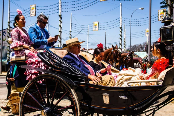 Seville, İspanya - 5 Mayıs 2022 Sevillianlar geleneksel Endülüs tarzında giyinmiş bir şekilde İspanya 'nın en ünlü festivali olan Feria de Sevilla' nın koridorlarında at arabasıyla dolaşıyorlar.