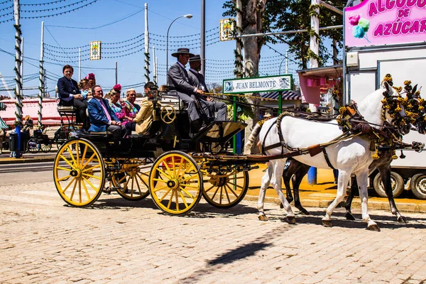 Seville, İspanya - 5 Mayıs 2022 Sevillianlar geleneksel Endülüs tarzında giyinmiş bir şekilde İspanya 'nın en ünlü festivali olan Feria de Sevilla' nın koridorlarında at arabasıyla dolaşıyorlar.