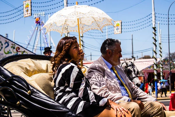 Seville, İspanya - 5 Mayıs 2022 Sevillianlar geleneksel Endülüs tarzında giyinmiş bir şekilde İspanya 'nın en ünlü festivali olan Feria de Sevilla' nın koridorlarında at arabasıyla dolaşıyorlar.