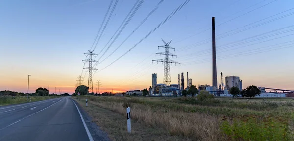 View of the road with power line and chemical factory with buildings and pipelines. Electricity grid expansion for the energy transition with chemical plant.