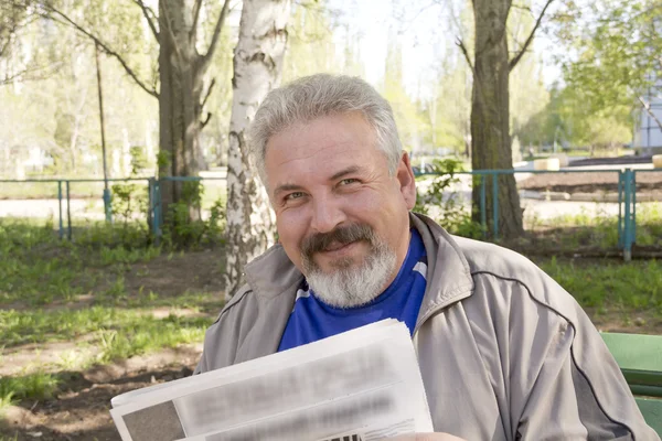 Um homem de meia idade lendo um jornal em um parque Imagens De Bancos De Imagens Sem Royalties