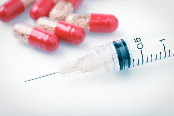 Píldoras rojas médicas y aguja de una jeringa — Foto de Stock