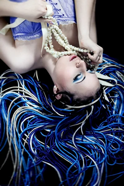 Готично виглядає жінка з синьо-білою зачіскою жаху з перловим намистом догори ногами на чорному тлі Ліцензійні Стокові Фото