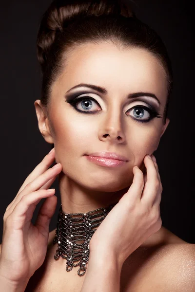 Gothic beautiful woman with giant pretty blue eyes and evening makeup on black background looking to the camera and holding her hands near her face — Stock Photo, Image