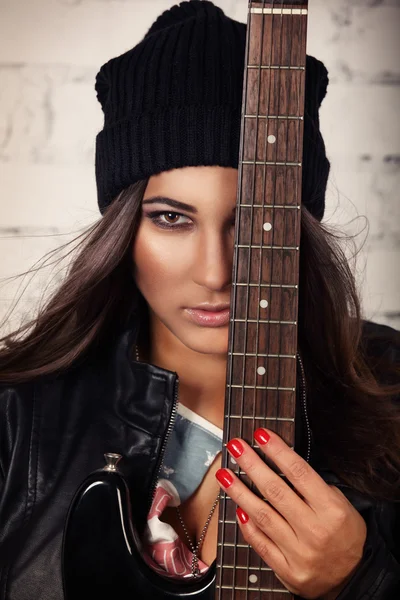 Fiducioso cercando femminile chitarra tenuta vicino al suo viso in piedi di fronte al muro di mattoni bianchi — Foto Stock