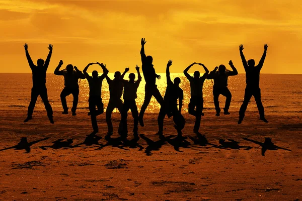 Male friends are having fun at summer and jumping up on the sunset near the sea putting their hands up to the orange sky — Stock Photo, Image