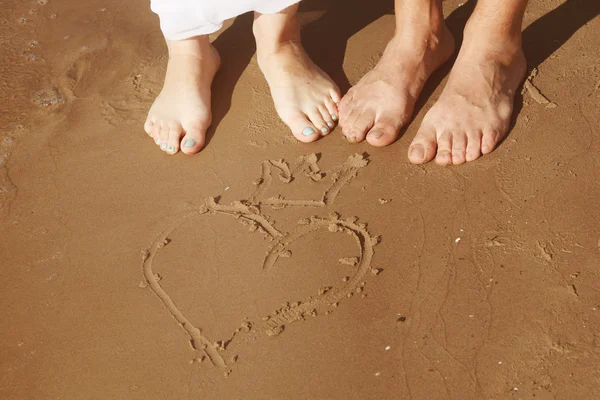 Pareja los pies de pie sobre la arena cerca del corazón y la corona — Foto de Stock